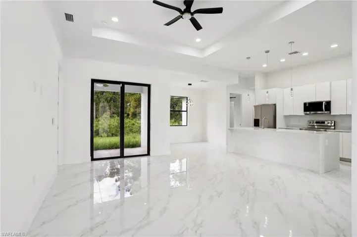 Kitchen featuring an island with sink, light tile flooring, pendant lighting, a raised ceiling, and appliances with stainless steel finishes