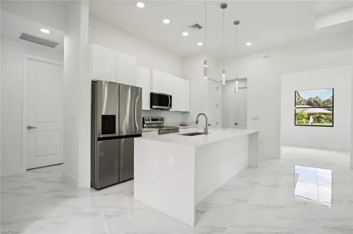 Kitchen featuring light tile flooring, stainless steel appliances, a center island with sink, sink, and pendant lighting