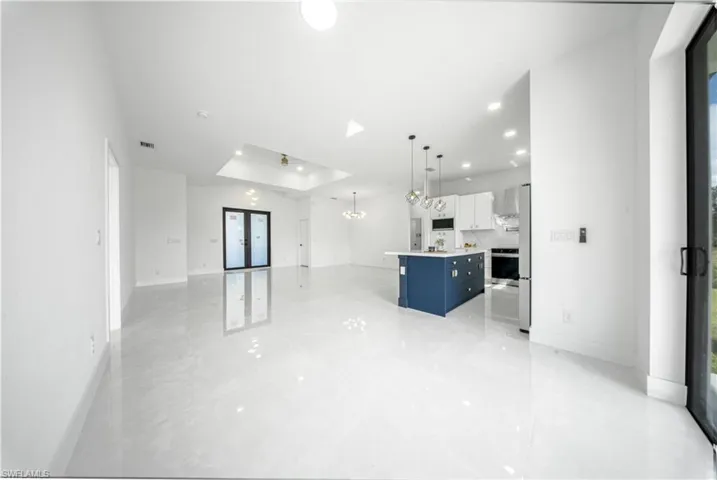 Unfurnished living room with a raised ceiling, french doors, recessed lighting, and a chandelier