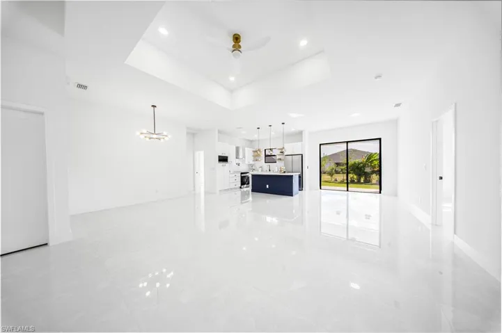 Unfurnished living room featuring a raised ceiling, ceiling fan, a chandelier, and recessed lighting