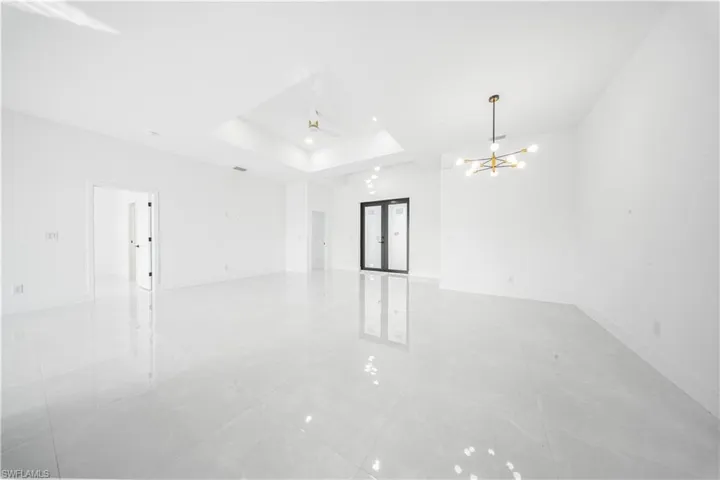 Empty room with french doors, a tray ceiling, and a chandelier