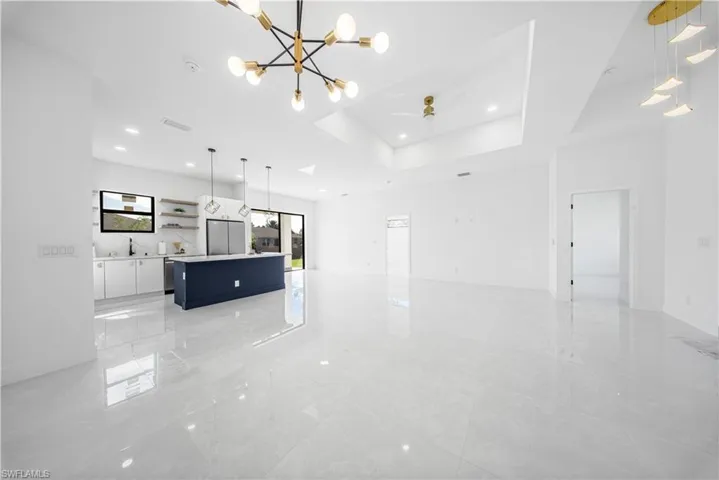 Unfurnished living room with a chandelier, a raised ceiling, a ceiling fan, and recessed lighting