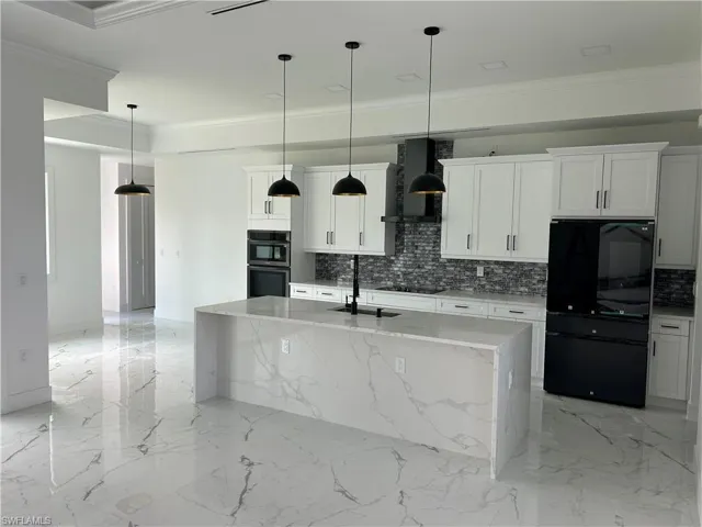 Kitchen featuring sink, decorative light fixtures, wall chimney exhaust hood, an island with sink, and black appliances