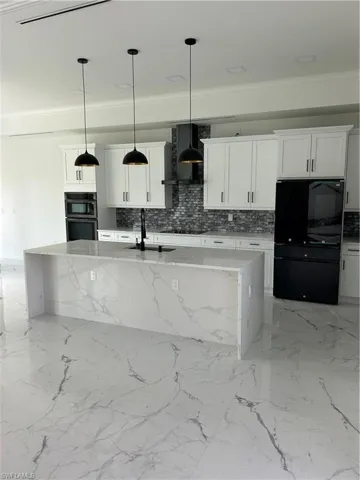 Kitchen with decorative backsplash, sink, a center island with sink, pendant lighting, and range hood