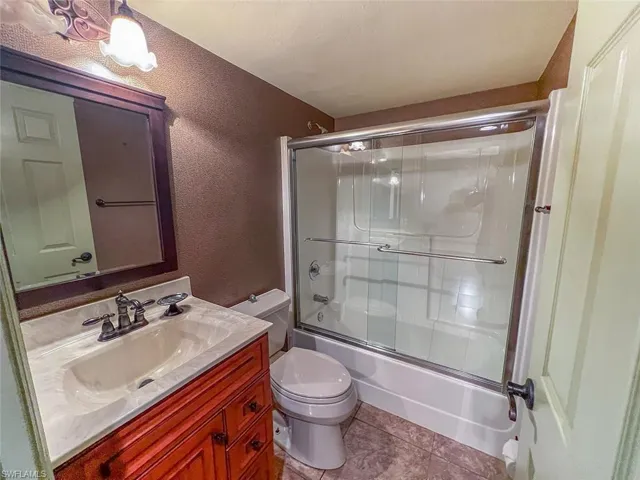 Full bathroom with toilet, vanity, bath / shower combo with glass door, a textured wall, and tile patterned floors