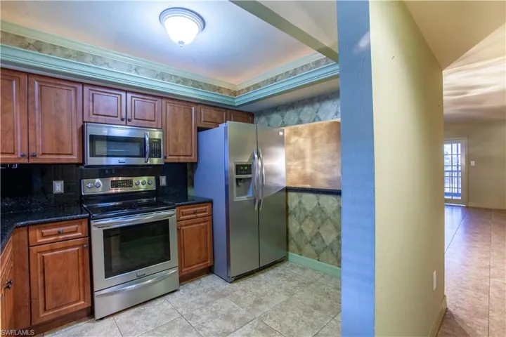 Kitchen with appliances with stainless steel finishes, light tile patterned floors, tasteful backsplash, and brown cabinets