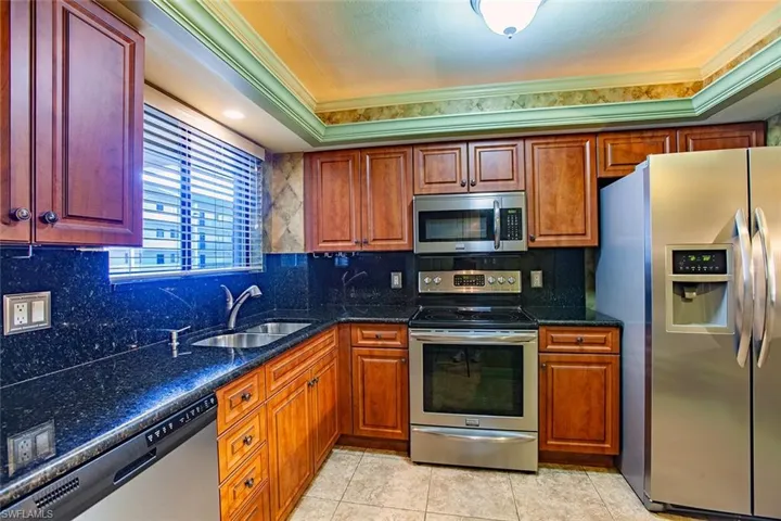 Kitchen with appliances with stainless steel finishes, a sink, crown molding, dark stone counters, and light tile patterned floors