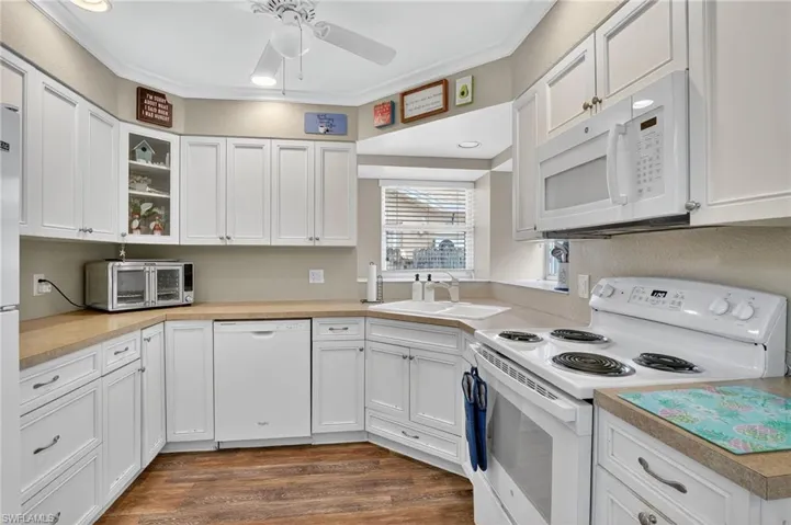 Kitchen with white appliances, white cabinets, light countertops, a ceiling fan, and dark wood-style floors