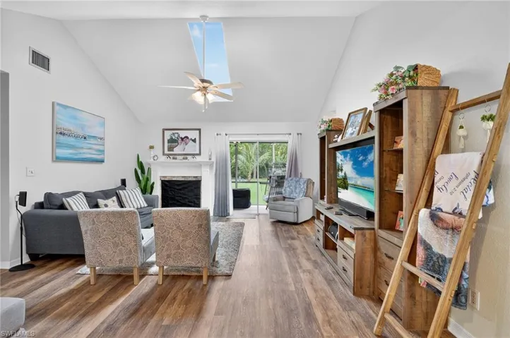 Living room featuring wood finished floors, ceiling fan, a fireplace, and high vaulted ceiling