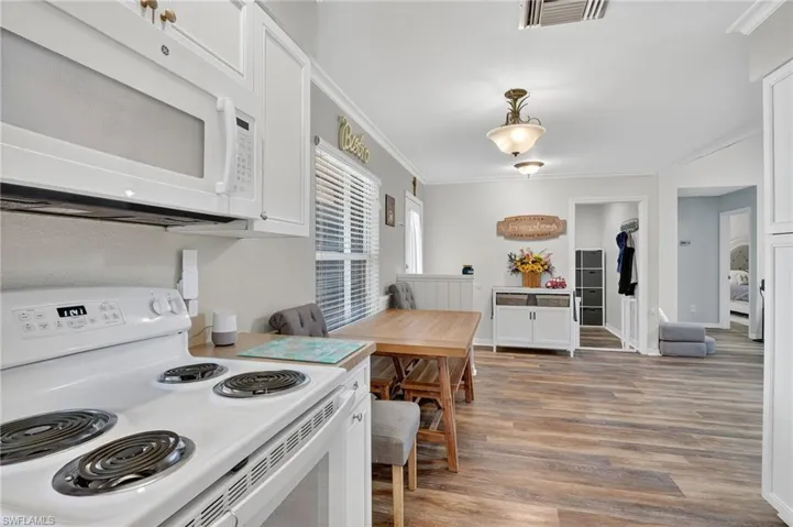 Kitchen featuring white appliances, ornamental molding, light wood-style flooring, white cabinetry, and pendant lighting