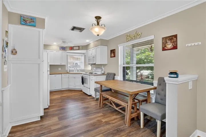 Kitchen with white appliances, plenty of natural light, white cabinets, crown molding, and dark wood-style floors
