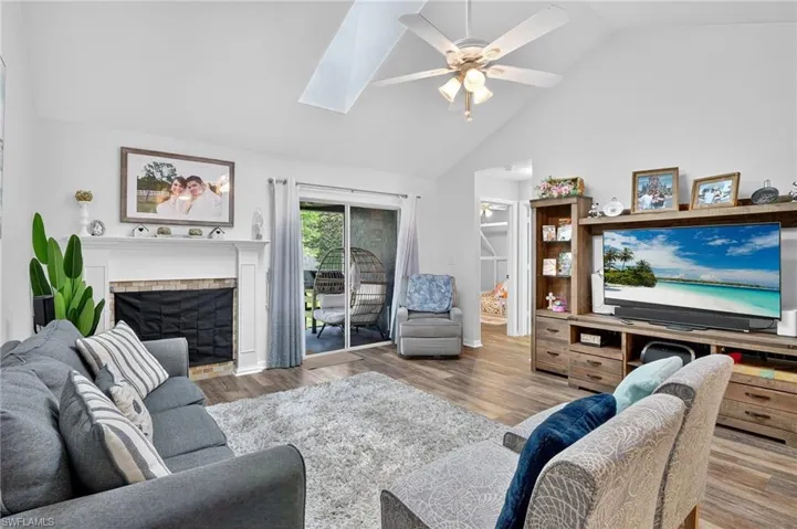Living area featuring ceiling fan, wood finished floors, high vaulted ceiling, a fireplace, and a skylight