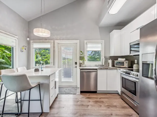 Kitchen featuring high vaulted ceiling, decorative light fixtures, appliances with stainless steel finishes, light hardwood / wood-style floors, and white cabinetry