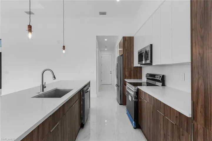 Kitchen featuring white cabinets, dark brown cabinets, sink, decorative light fixtures, and stainless steel appliances