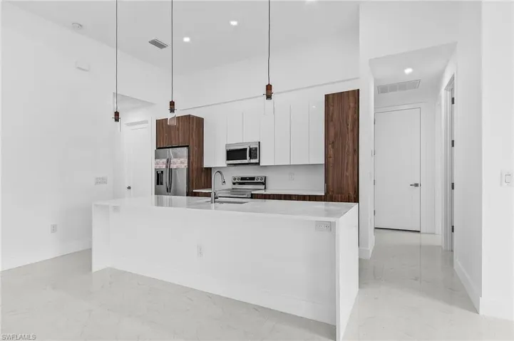 Kitchen with an island with sink, hanging light fixtures, sink, white cabinetry, and appliances with stainless steel finishes