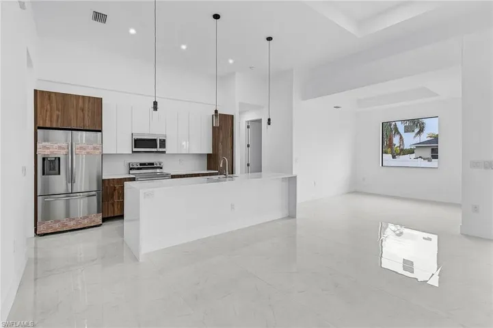 Kitchen featuring appliances with stainless steel finishes, sink, hanging light fixtures, white cabinetry, and a kitchen island with sink