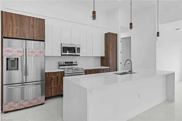 Kitchen with stainless steel appliances, hanging light fixtures, sink, and white cabinets