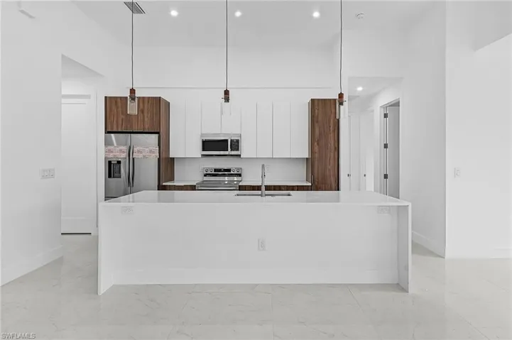 Kitchen featuring white cabinets, hanging light fixtures, an island with sink, appliances with stainless steel finishes, and sink