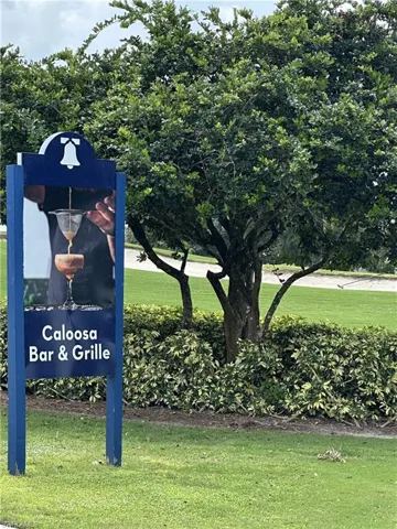 Caloosa Bar & Grille signage featuring a cocktail image and bell motif, surrounded by mature trees, lush green grass, and manicured shrubbery