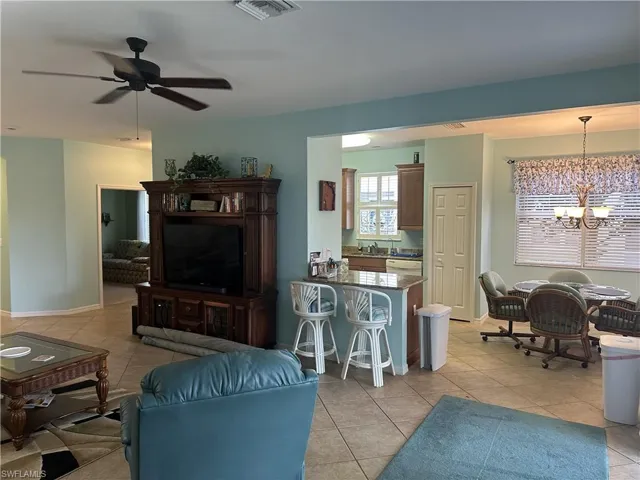 Open-concept living area with tile flooring throughout, featuring a kitchen pass-through with a breakfast bar, a dedicated dining area with a chandelier, and a ceiling fan in the main living space