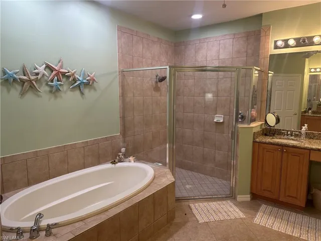 Spacious bathroom featuring a built-in soaking tub, a separate glass-enclosed shower with tile surround, a single vanity with stone-finish countertop, and integrated ceiling lighting