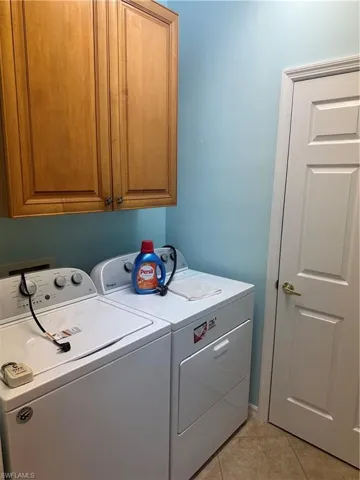 Dedicated laundry space featuring upper cabinetry, white paneled door, and tile flooring