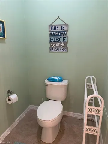 Powder room featuring light green walls, a white toilet, and neutral-toned tile flooring