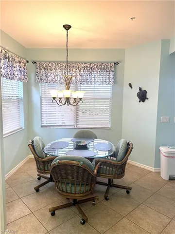 Bright dining area featuring tile flooring, dual windows with blinds, a multi-bulb chandelier, and light blue wall tones