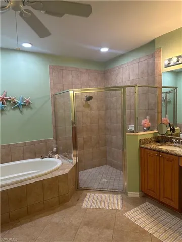 Spacious bathroom featuring a corner walk-in shower with glass enclosure, a built-in soaking tub, tile flooring, a dual-sink vanity with stone countertop, and recessed lighting