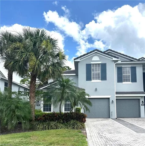 Stucco exterior featuring dark blue shutters, a tiled roof, and a paver driveway