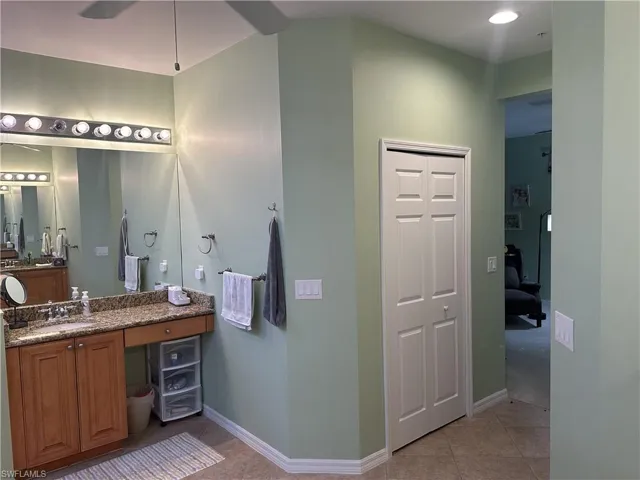 Bathroom vanity with granite countertop, wood cabinetry, and a full-width mirror with overhead fixture lighting