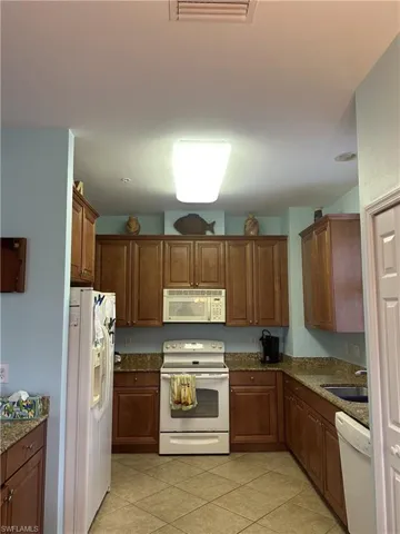 Kitchen featuring wood-finish cabinetry, patterned stone-finish countertops, and a full suite of white appliances including a range, built-in microwave, and refrigerator
