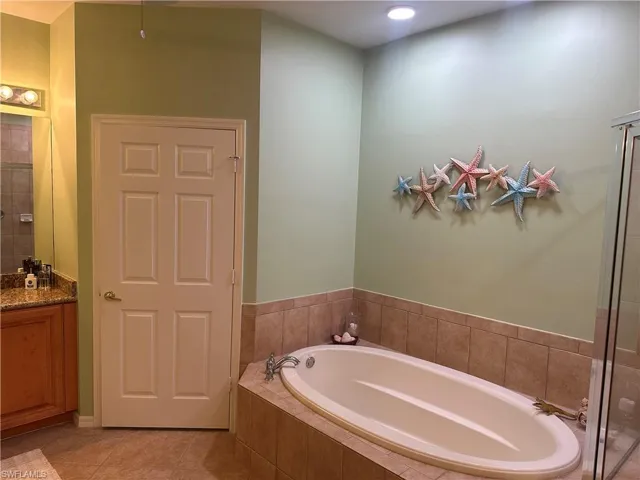 Garden tub with tiled surround, recessed lighting, and a glass-enclosed shower