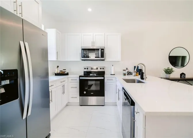 Kitchen with white cabinetry, kitchen peninsula, stainless steel appliances, and sink