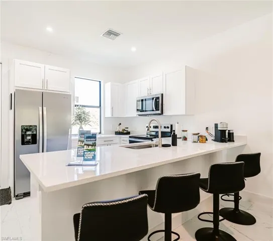 Kitchen with white cabinets, appliances with stainless steel finishes, kitchen peninsula, and a kitchen breakfast bar