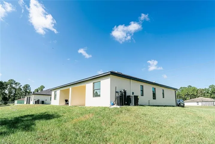 Rear view of house featuring central air condition unit and a lawn