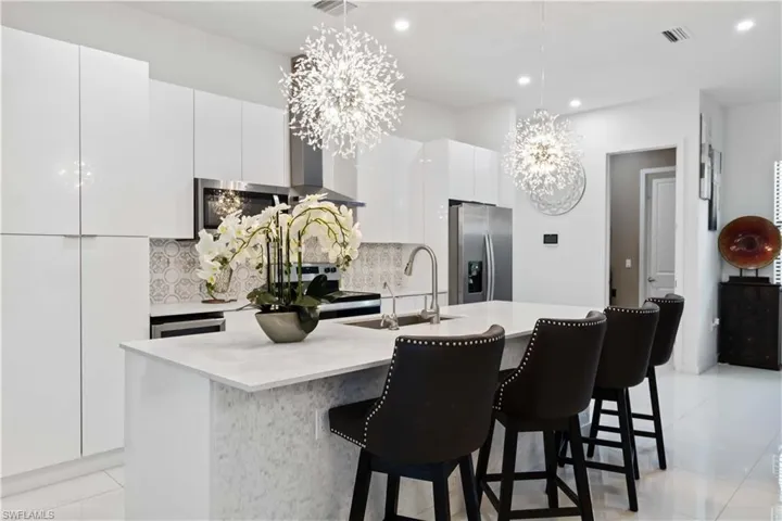 Kitchen with a center island with sink, light tile patterned floors, stainless steel fridge, white cabinets, and a chandelier