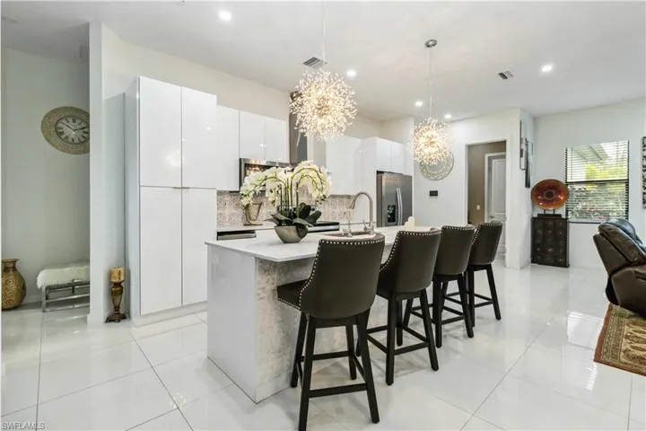 Kitchen featuring white cabinets, stainless steel refrigerator with ice dispenser, decorative light fixtures, backsplash, and a center island with sink