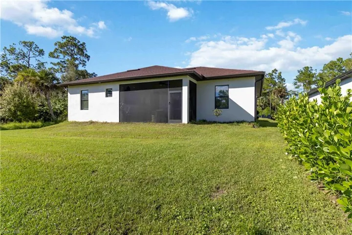 Rear view of house with a yard, stucco siding, and a sunroom