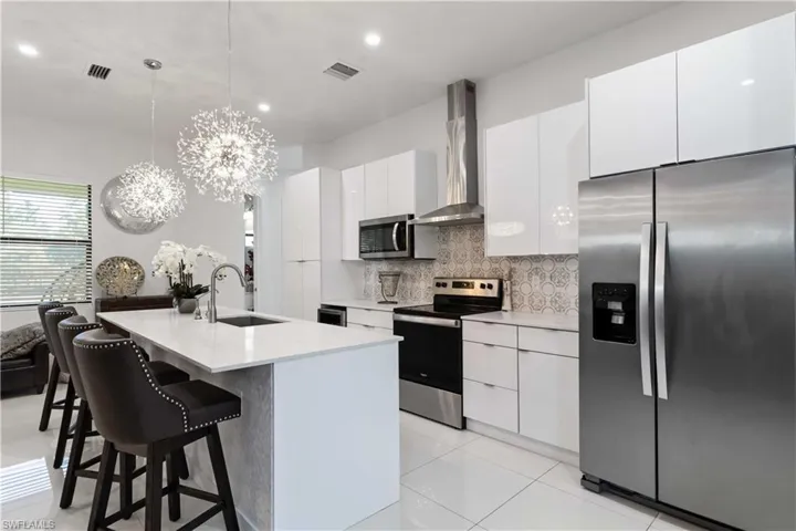 Kitchen with stainless steel appliances, pendant lighting, backsplash, a chandelier, and wall chimney range hood