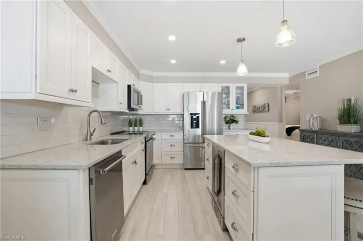 Kitchen featuring appliances with stainless steel finishes, light stone counters, white cabinets, pendant lighting, and tasteful backsplash