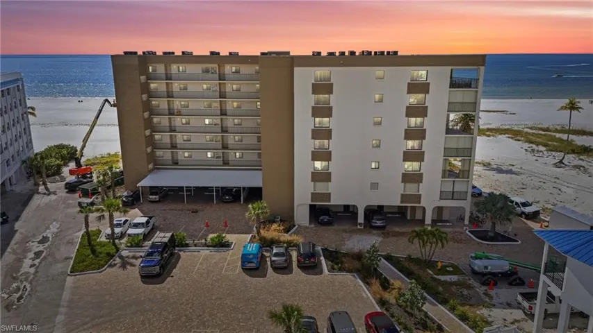Property at dusk featuring a view of apartment building / complex, view of water and beach, and uncovered parking