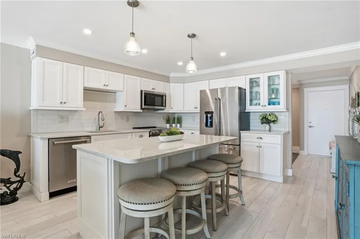 Kitchen with tasteful backsplash, decorative light fixtures, white cabinetry, a breakfast bar, and crown molding