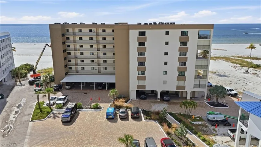 View of apartment building / complex featuring view of water and beach and uncovered parking