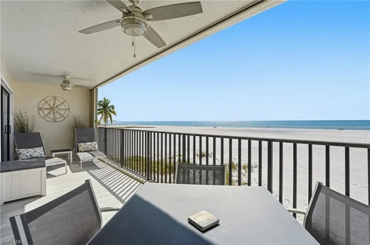 Balcony featuring view of water and beach, outdoor dining space, and ceiling fan