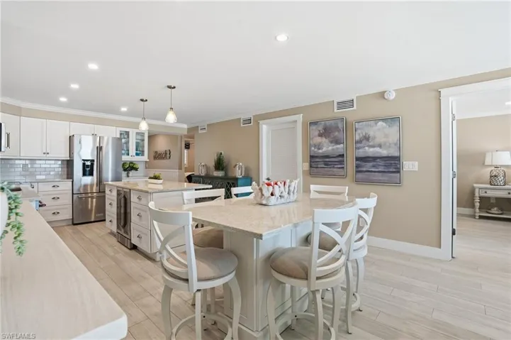 Kitchen with a kitchen island, a kitchen breakfast bar, white cabinetry, stainless steel refrigerator with ice dispenser, and recessed lighting