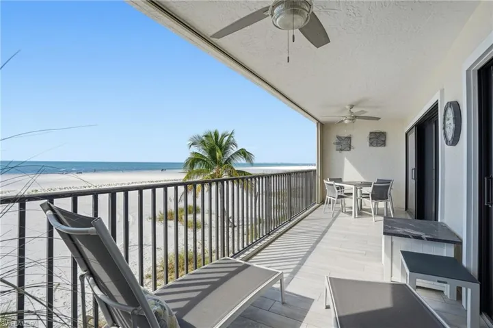 Balcony with outdoor dining space, ceiling fan, and view of water and beach