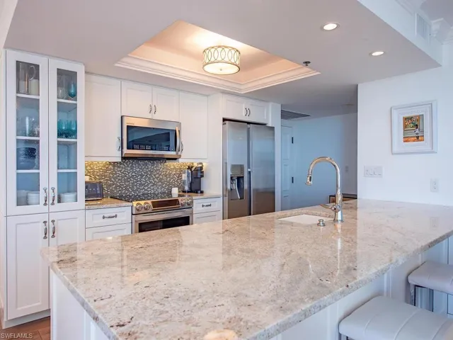 Kitchen featuring a peninsula, a tray ceiling, light stone countertops, white cabinets, and recessed lighting