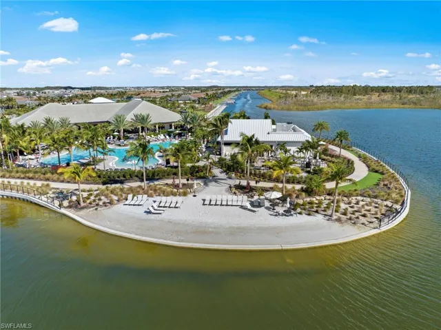 Expansive resort-style pool area with multiple buildings, surrounding water features, sandy beach, and established palm trees