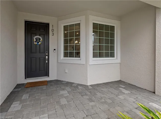 Entryway featuring textured stucco siding, a paneled front door with modern hardware, and a bay window with grid-patterned panes